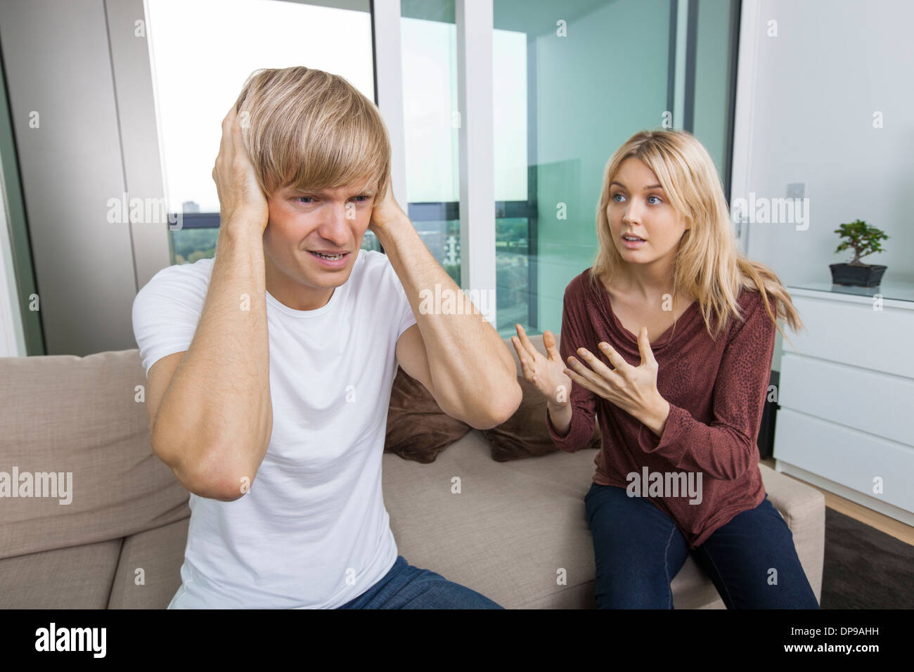 Woman trying to talk as man yells out aloud in living room at home Stock Photo