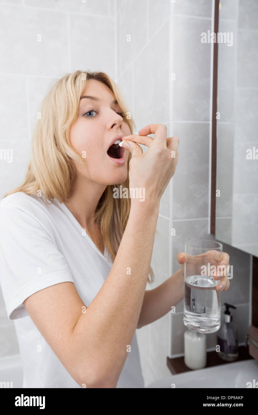 Young woman taking medicine in bathroom Stock Photo