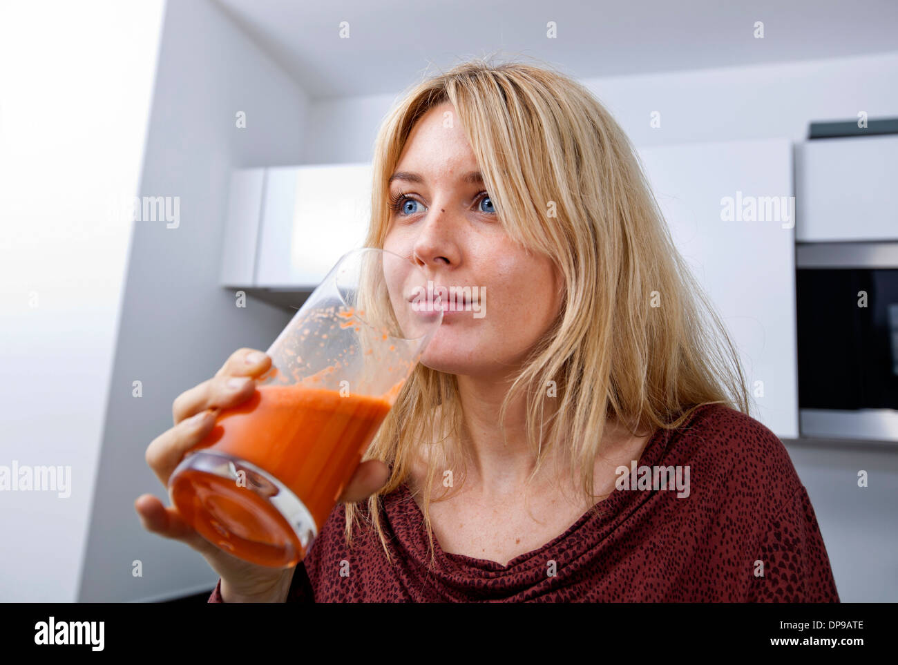 Young woman drinking carrot juice in kitchen Stock Photo