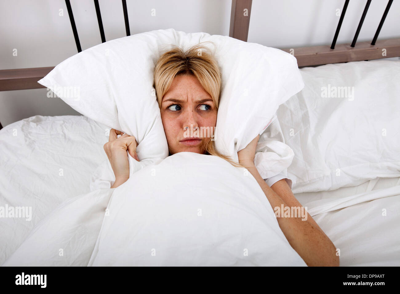 Young woman covering ears with pillow in bed Stock Photo