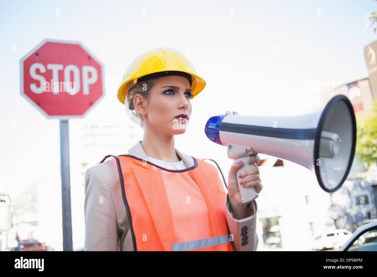 Frowning businesswoman wearing builders clothes holding megaphone Stock Photo