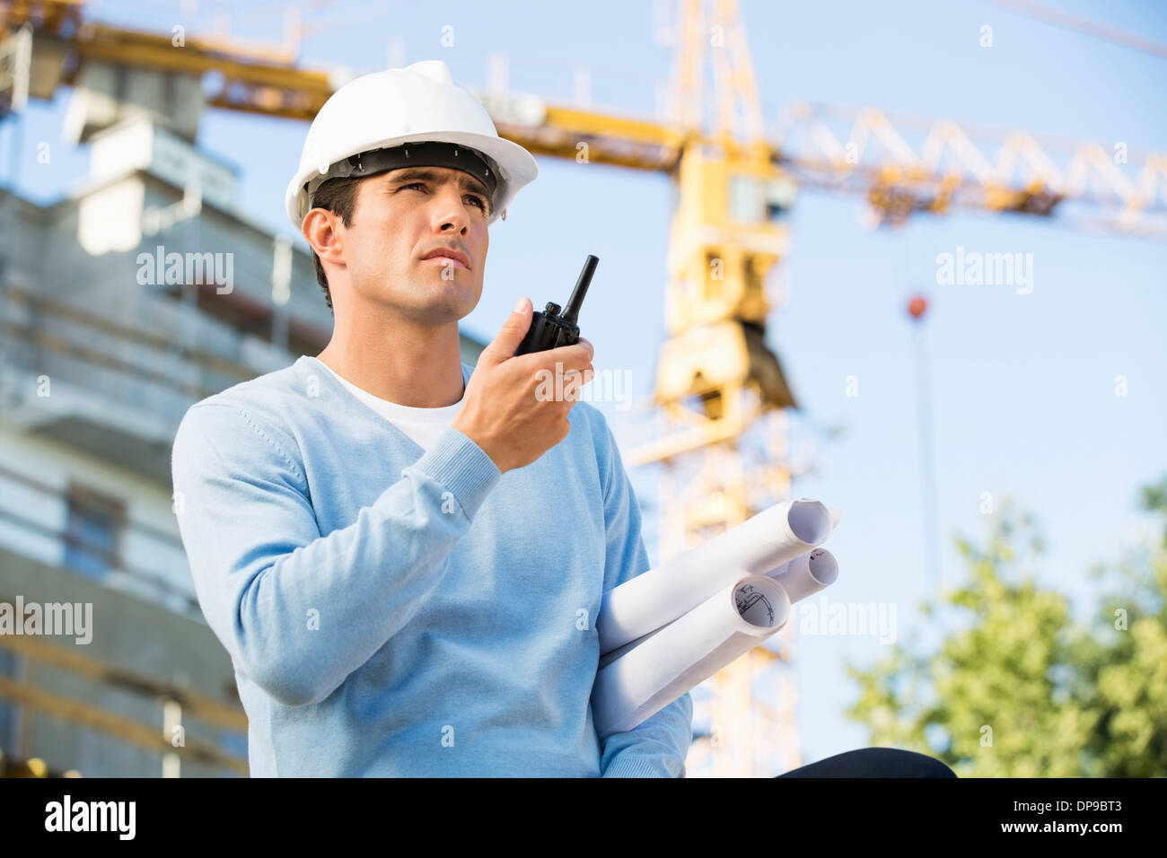 Male architect with blueprints using walkie-talkie at construction site Stock Photo