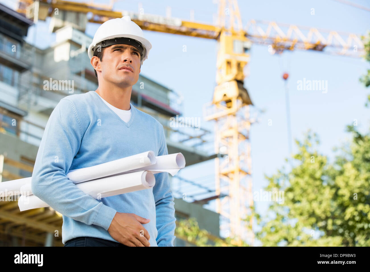 Male architect holding rolled up blueprints while standing at construction site Stock Photo