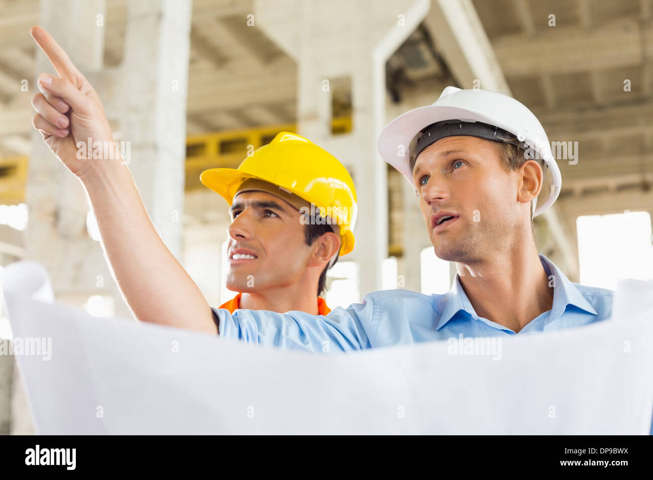 Male architect explaining building plan to colleague at construction ...