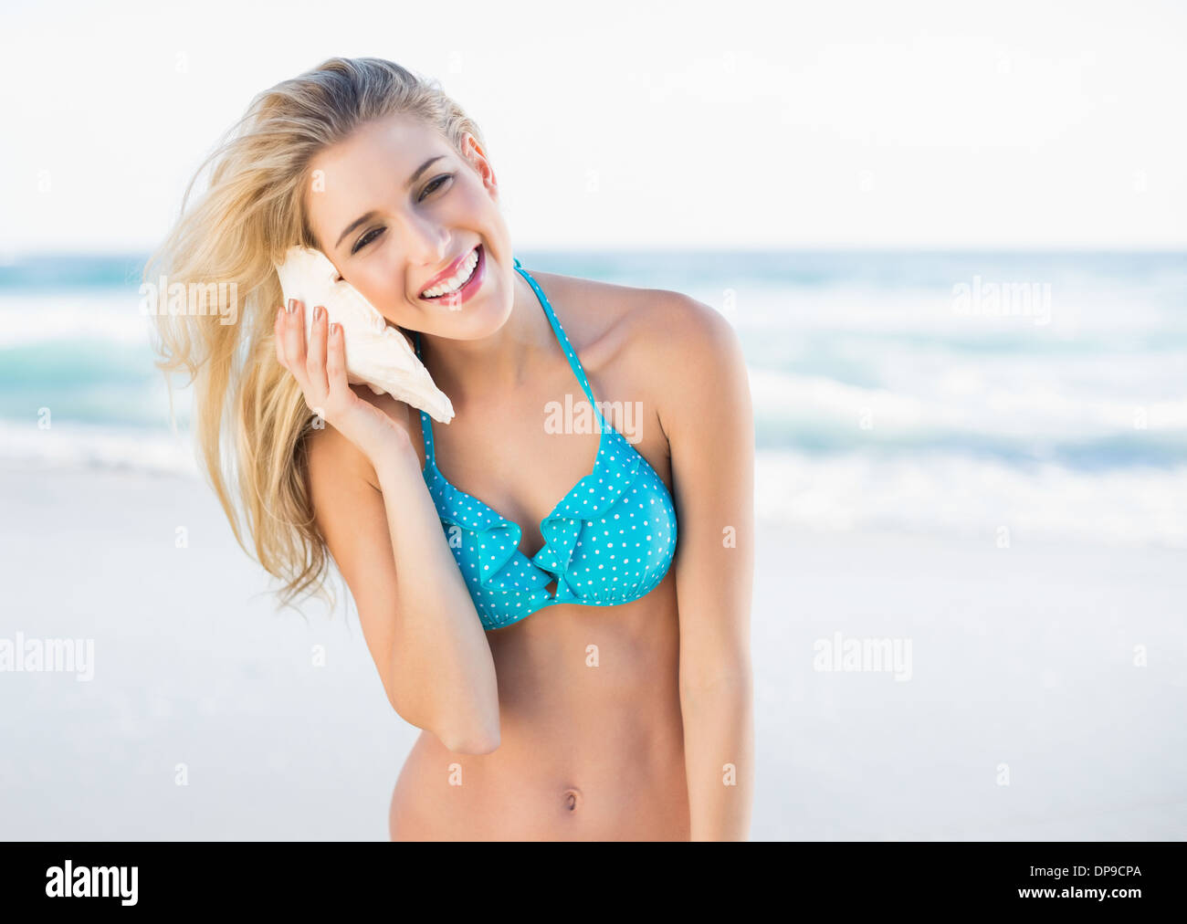 Cheerful gorgeous blonde in bikini holding shell by her ear Stock Photo