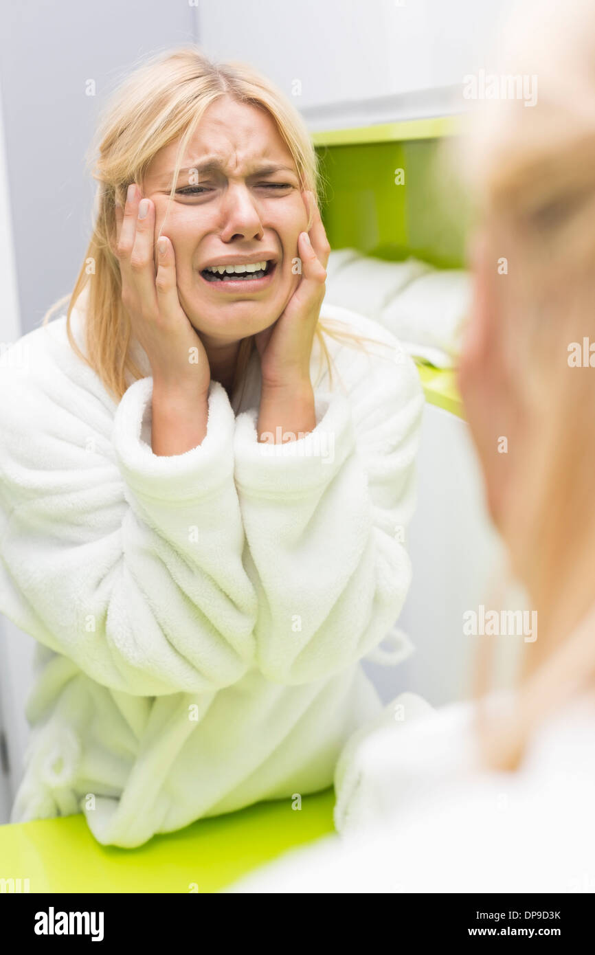 Young ill woman crying while looking at mirrior in bathroom Stock Photo