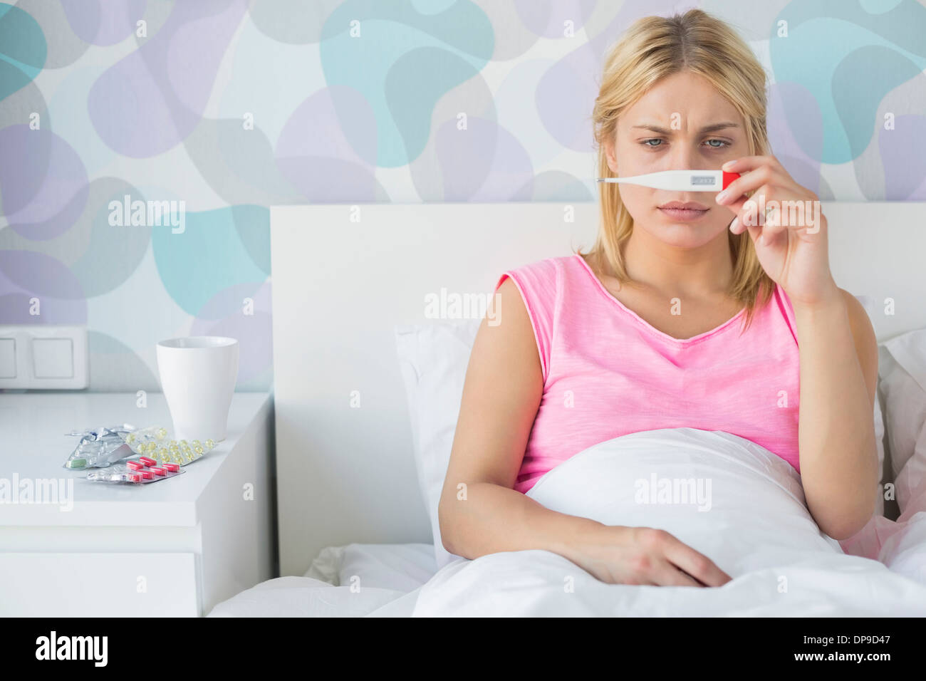Sick young woman taking temperature with thermometer in bed Stock Photo