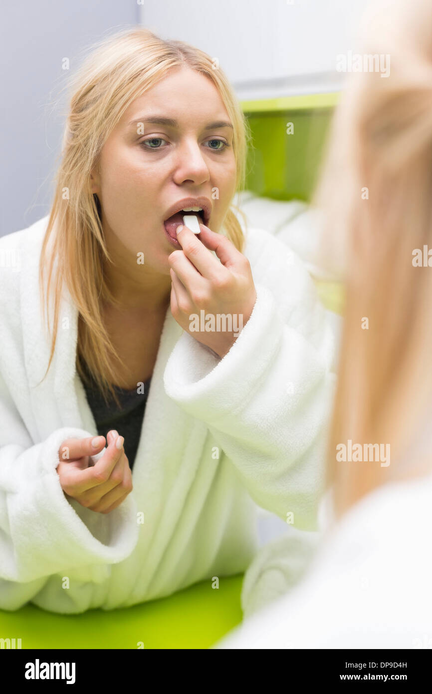 Young woman taking medicine while looking at mirror Stock Photo