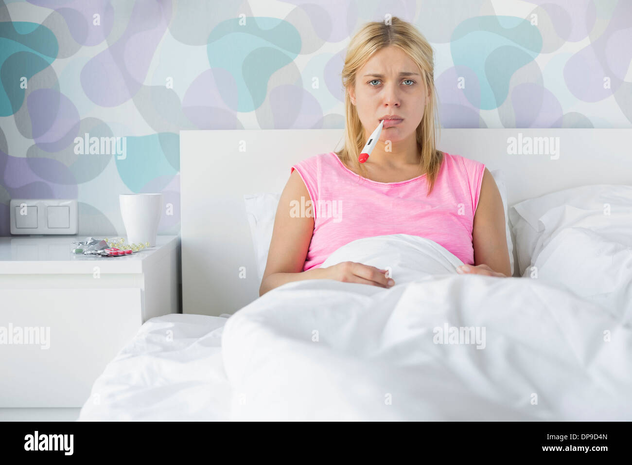 Portrait of young woman taking temperature with thermometer Stock Photo