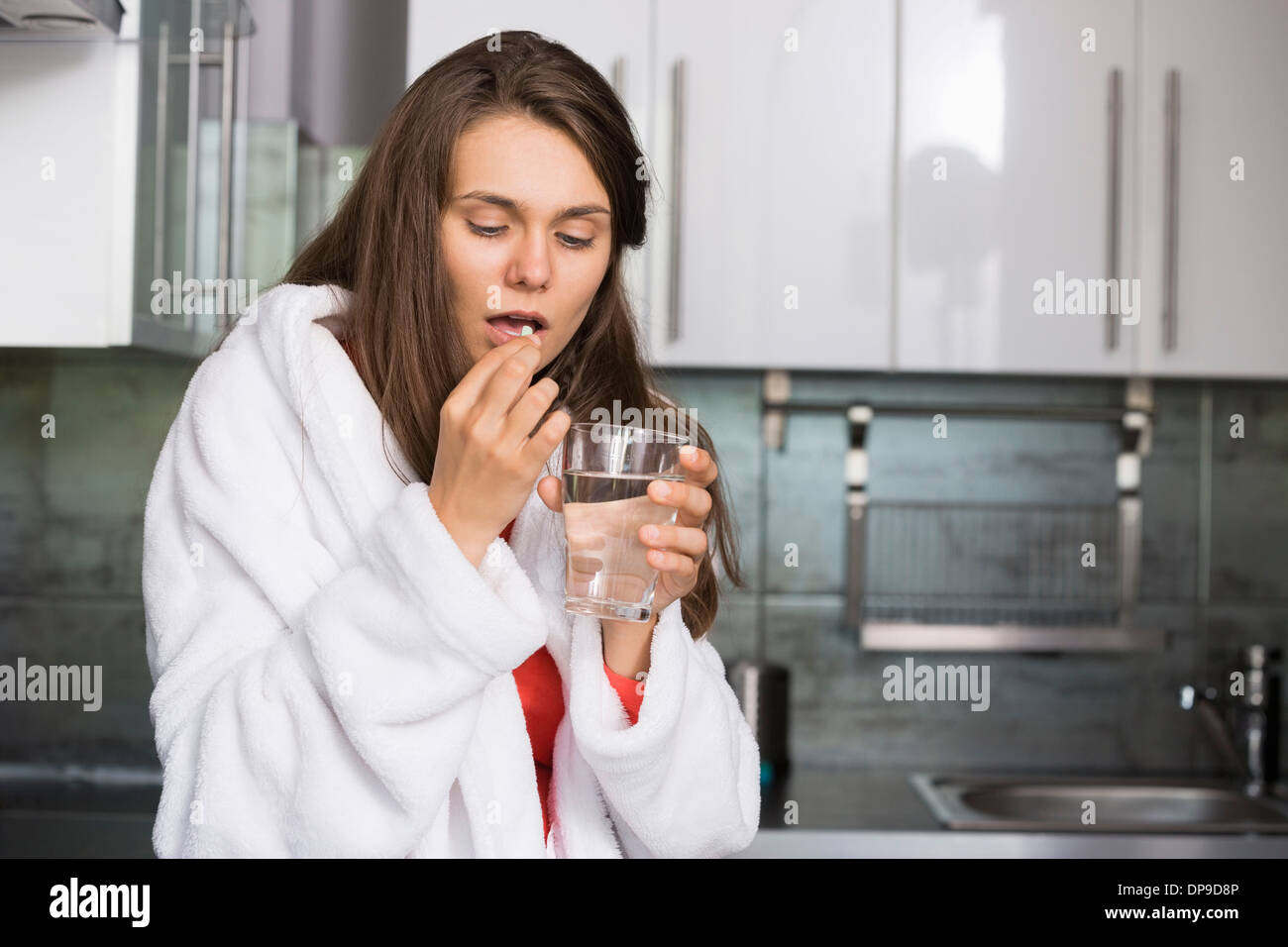 Ill woman taking medicine in kitchen Stock Photo