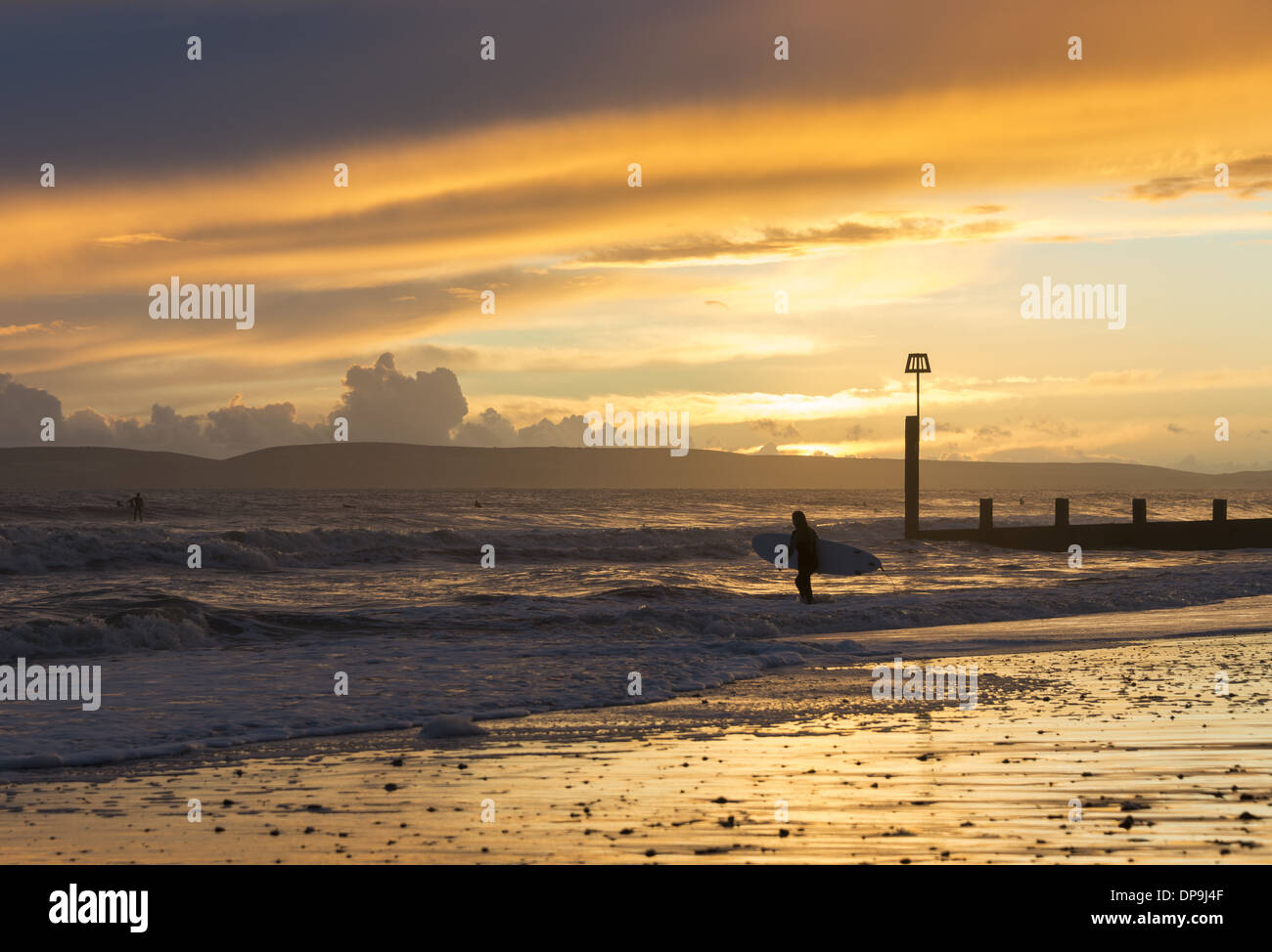 Surfer walking into the sea with surfboard at sunset on Boscombe beach in Dorset, England, UK Stock Photo