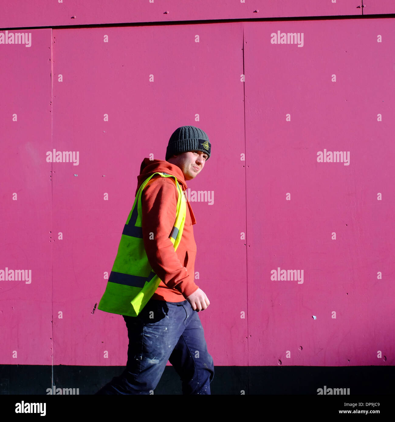 man wearing High Visibility jacket walking past pink site boarding Stock Photo