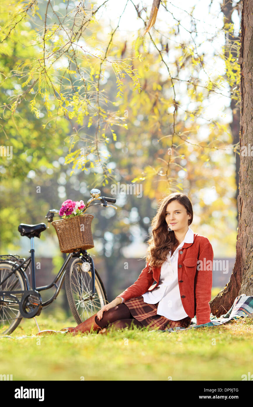Beautiful young female with bicycle sitting in park Stock Photo
