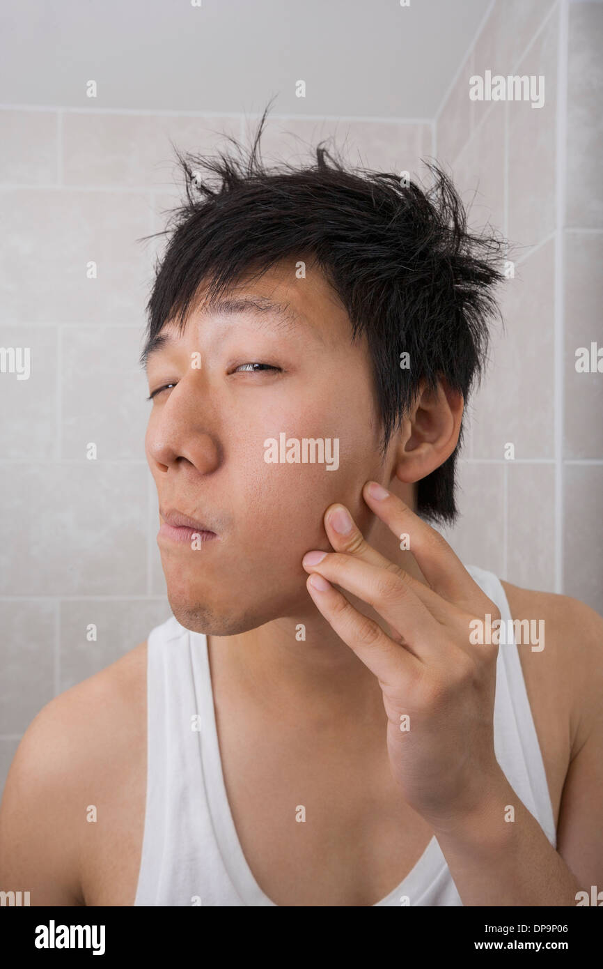 Asian mid adult man examining his face in bathroom Stock Photo