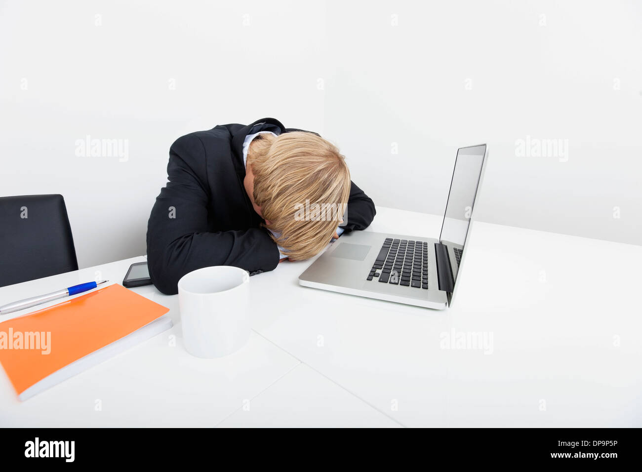 Mid adult businessman sleeping by laptop at desk in office Stock Photo