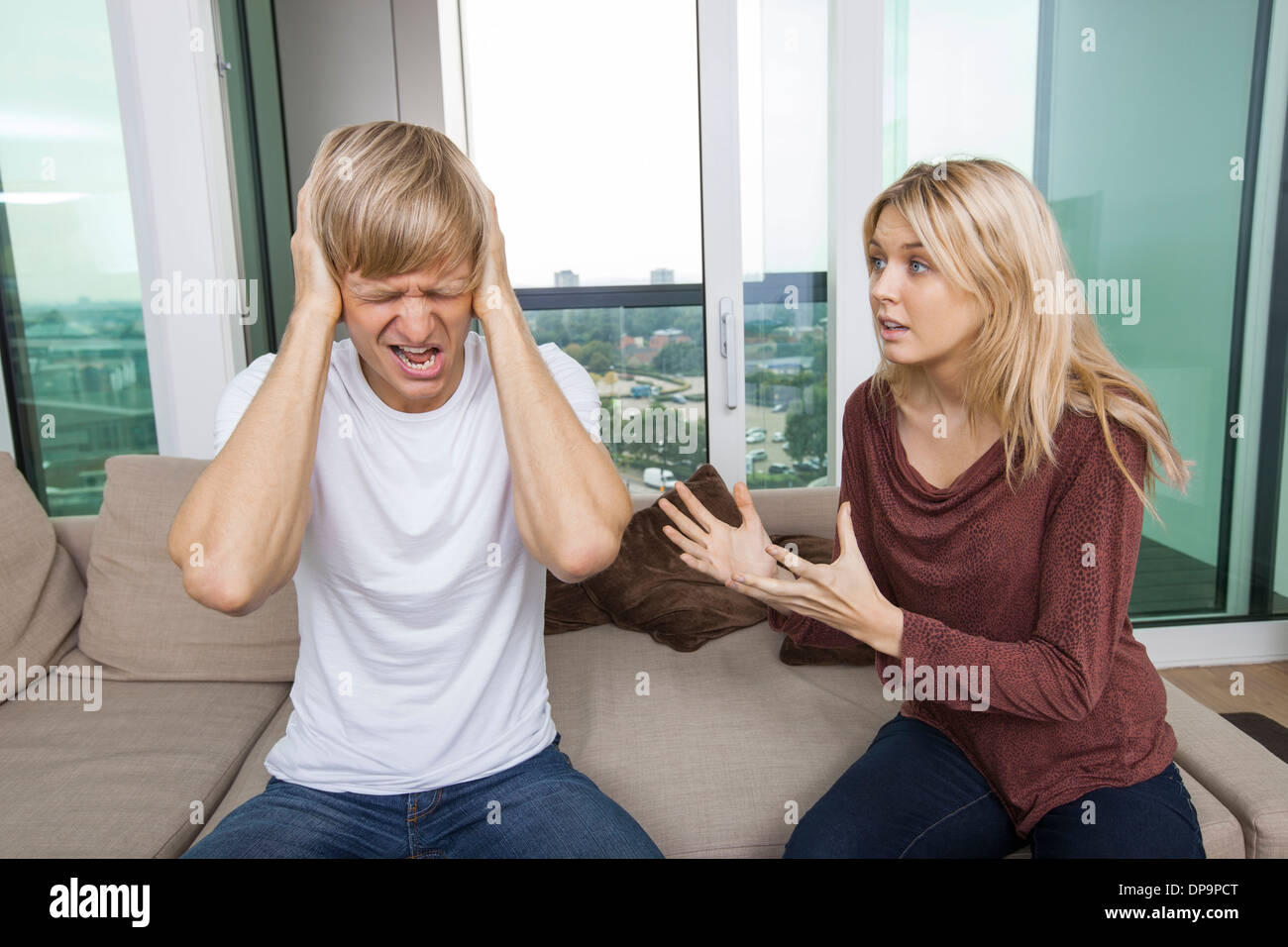 Woman trying to talk as man yells out aloud in living room at home Stock Photo