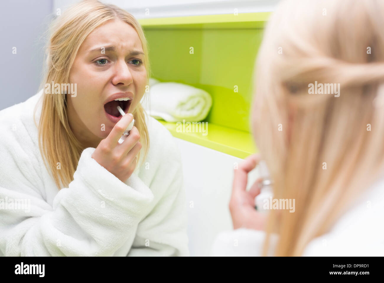 Reflection of woman spraying medicine in mouth Stock Photo
