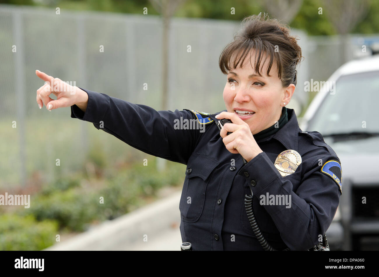 a female police officer talks on the radio with her patrol car in the background. Stock Photo