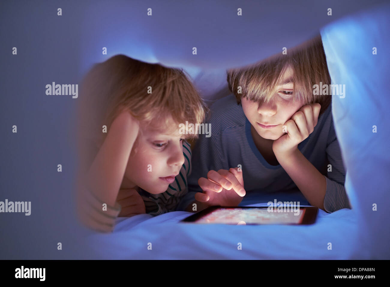 Brothers underneath duvet using digital tablet Stock Photo