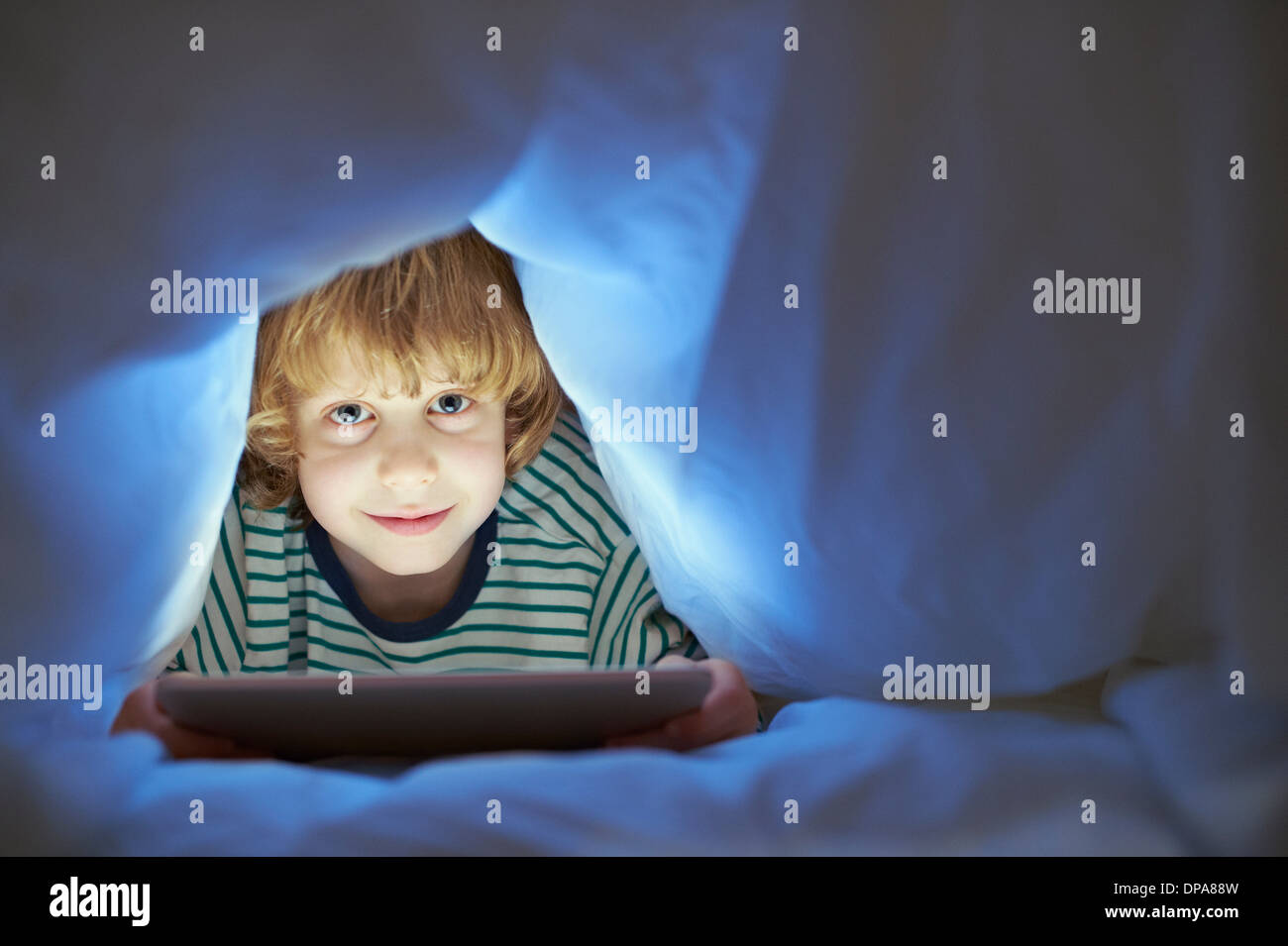 Boy underneath duvet using digital tablet Stock Photo