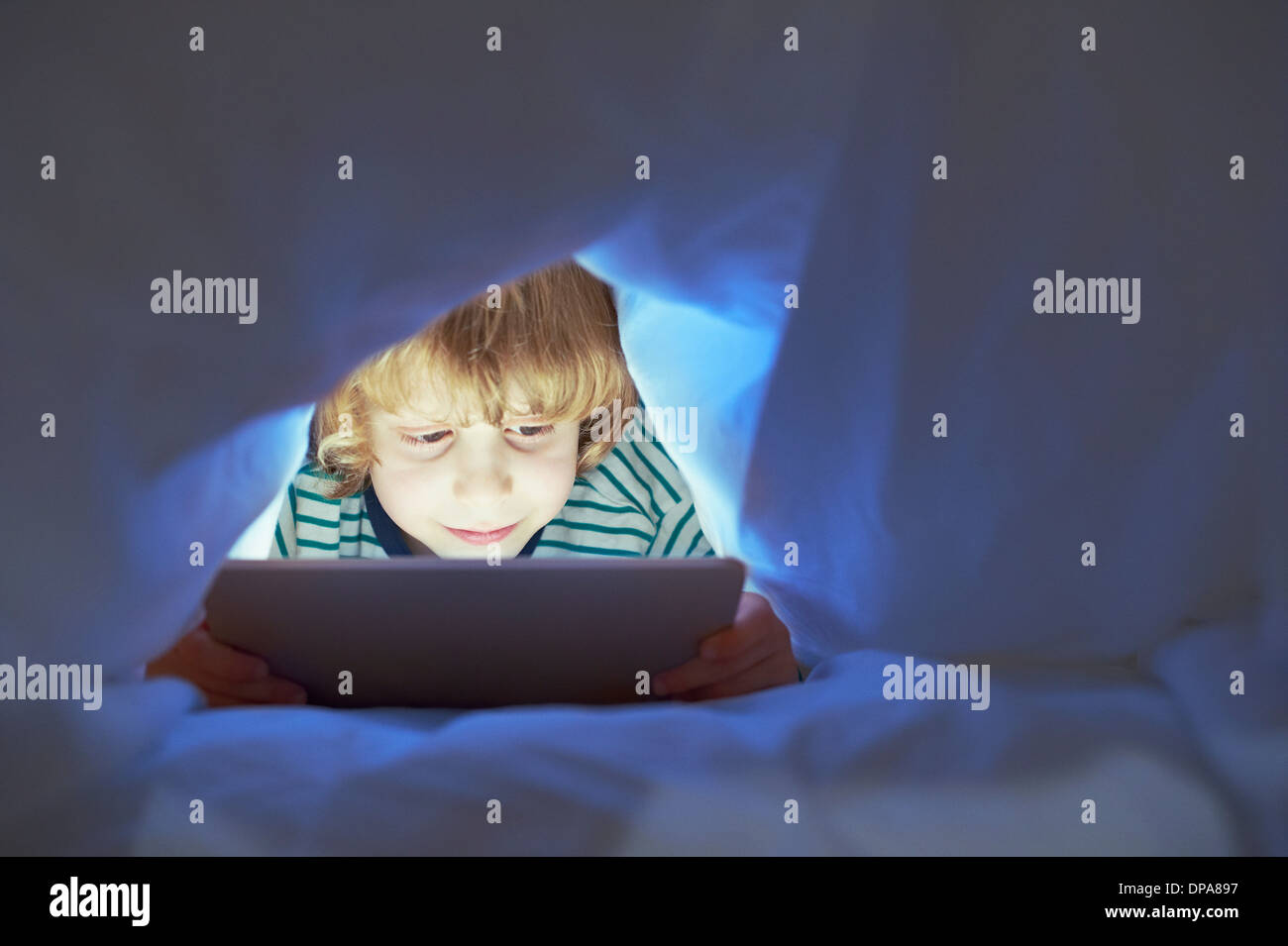 Boy underneath duvet using digital tablet Stock Photo