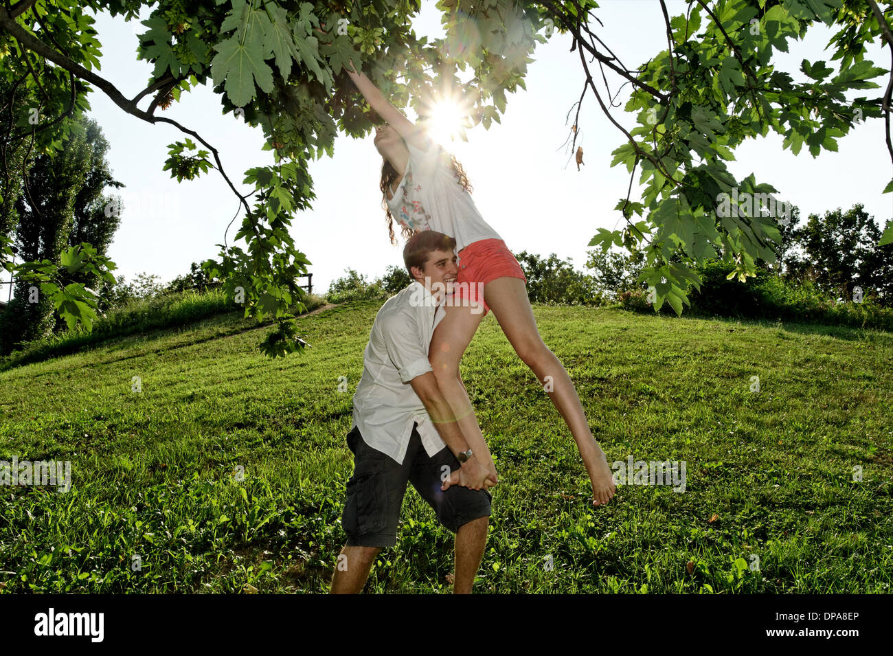 Young man lifting young woman to tree branches Stock Photo