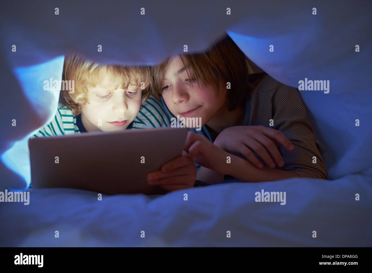 Brothers underneath duvet using digital tablet Stock Photo