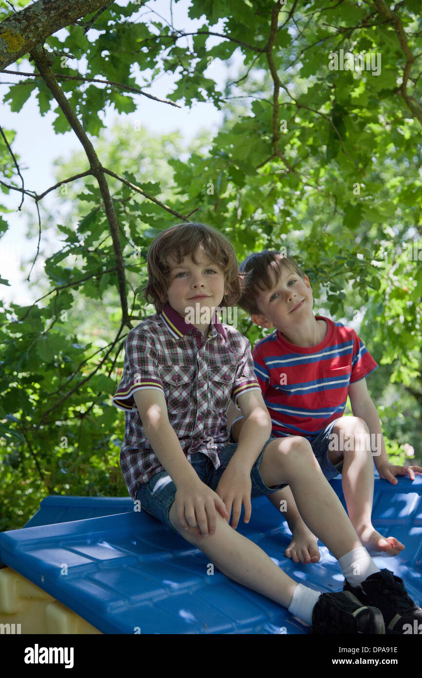 Boys sitting on roof of tree house Stock Photo