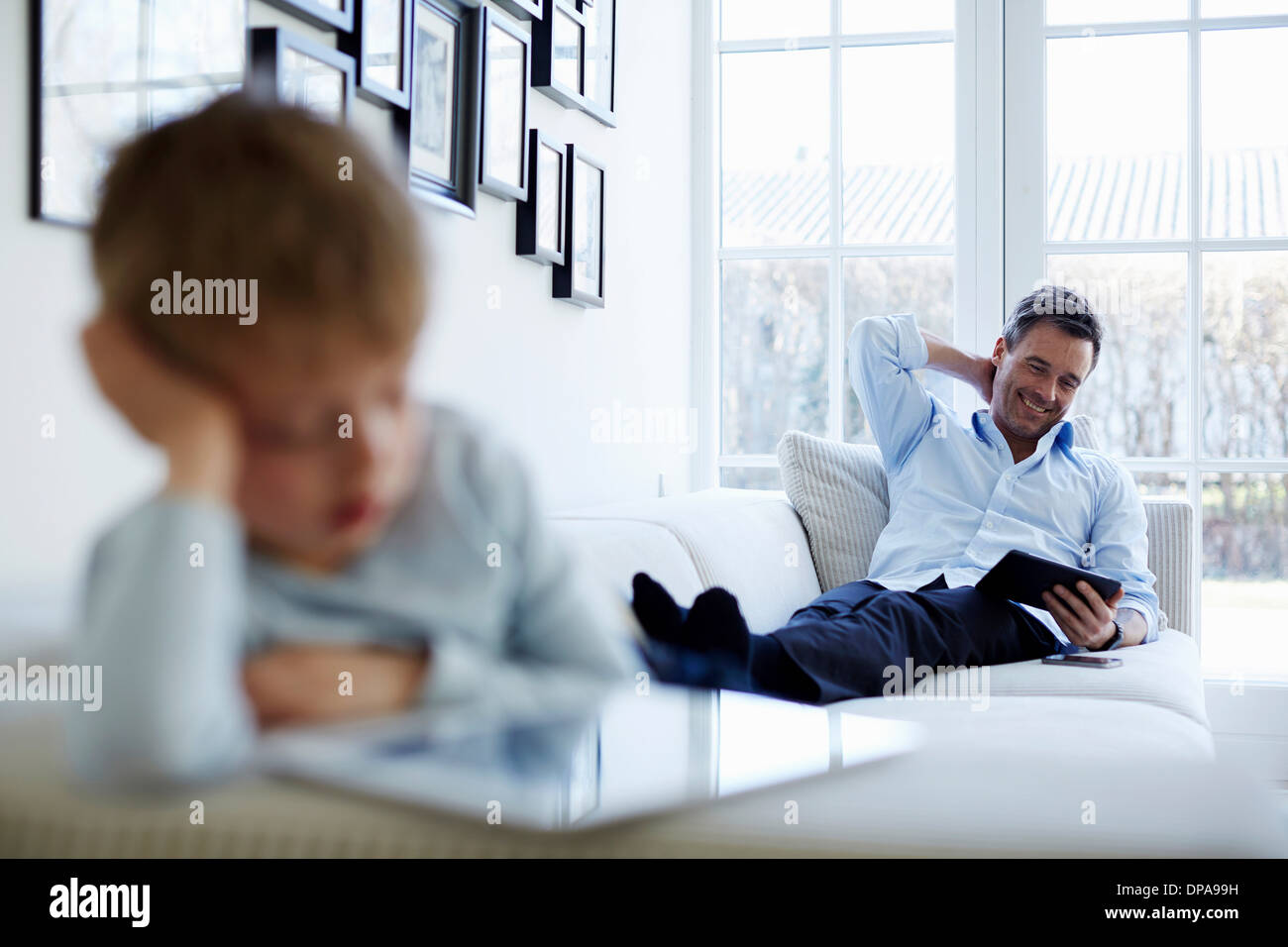 Father and son sitting on sofa using digital tablets Stock Photo