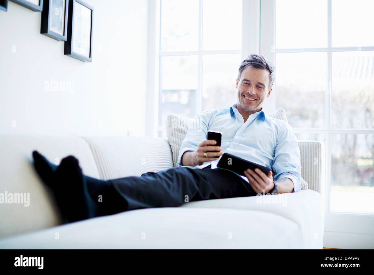 Man relaxing on sofa using digital tablet and smartphone Stock Photo