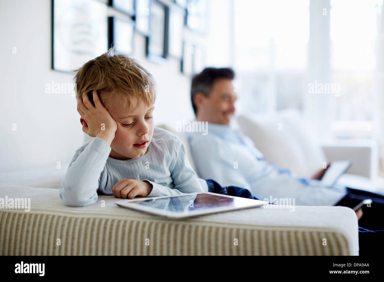 Father and son sitting on sofa using digital tablets Stock Photo