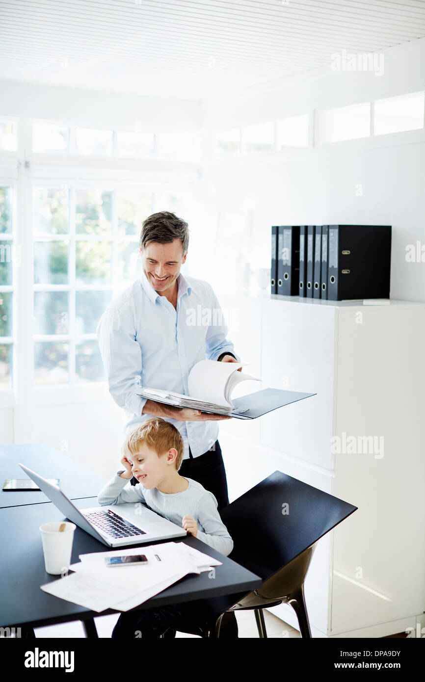 Boy using laptop and man looking at paperwork Stock Photo