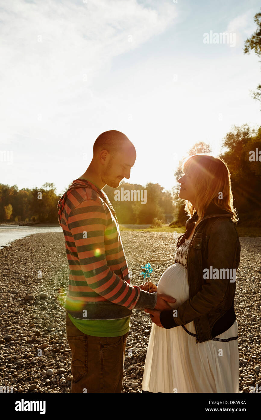 Pregnant woman and partner standing face to face beside river holding windmill Stock Photo