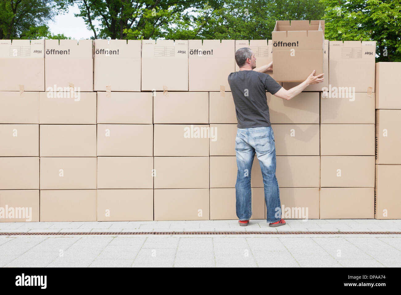 Man building wall of cardboard boxes Stock Photo