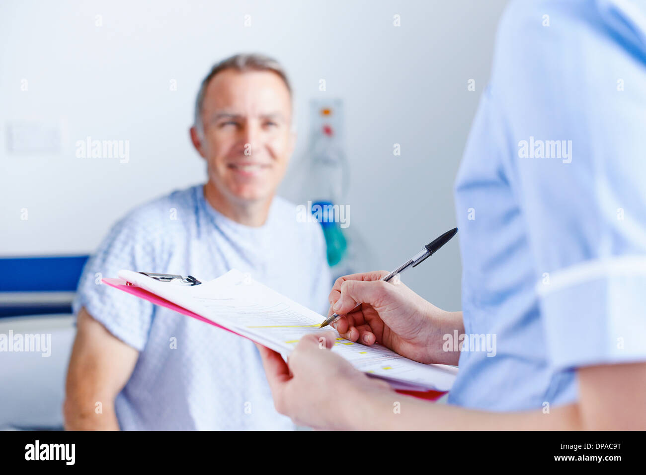 Nurse completing paperwork, patient in background Stock Photo - Alamy