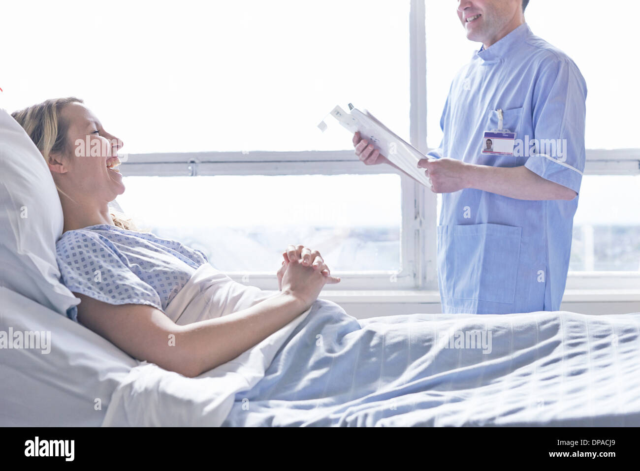 Patient lying in hospital bed laughing with nurse Stock Photo