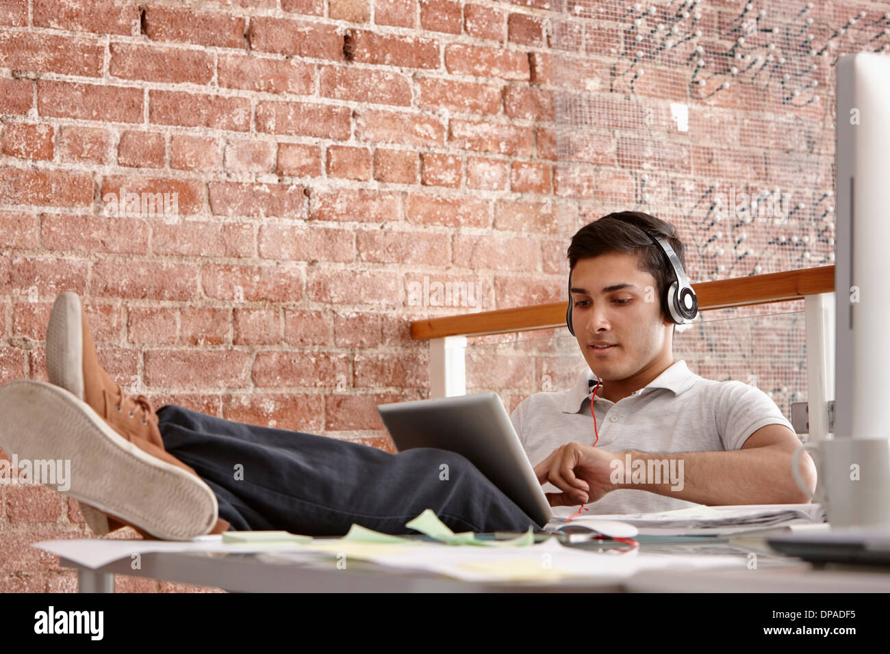 Young man using digital tablet wearing headphones, feet up Stock Photo