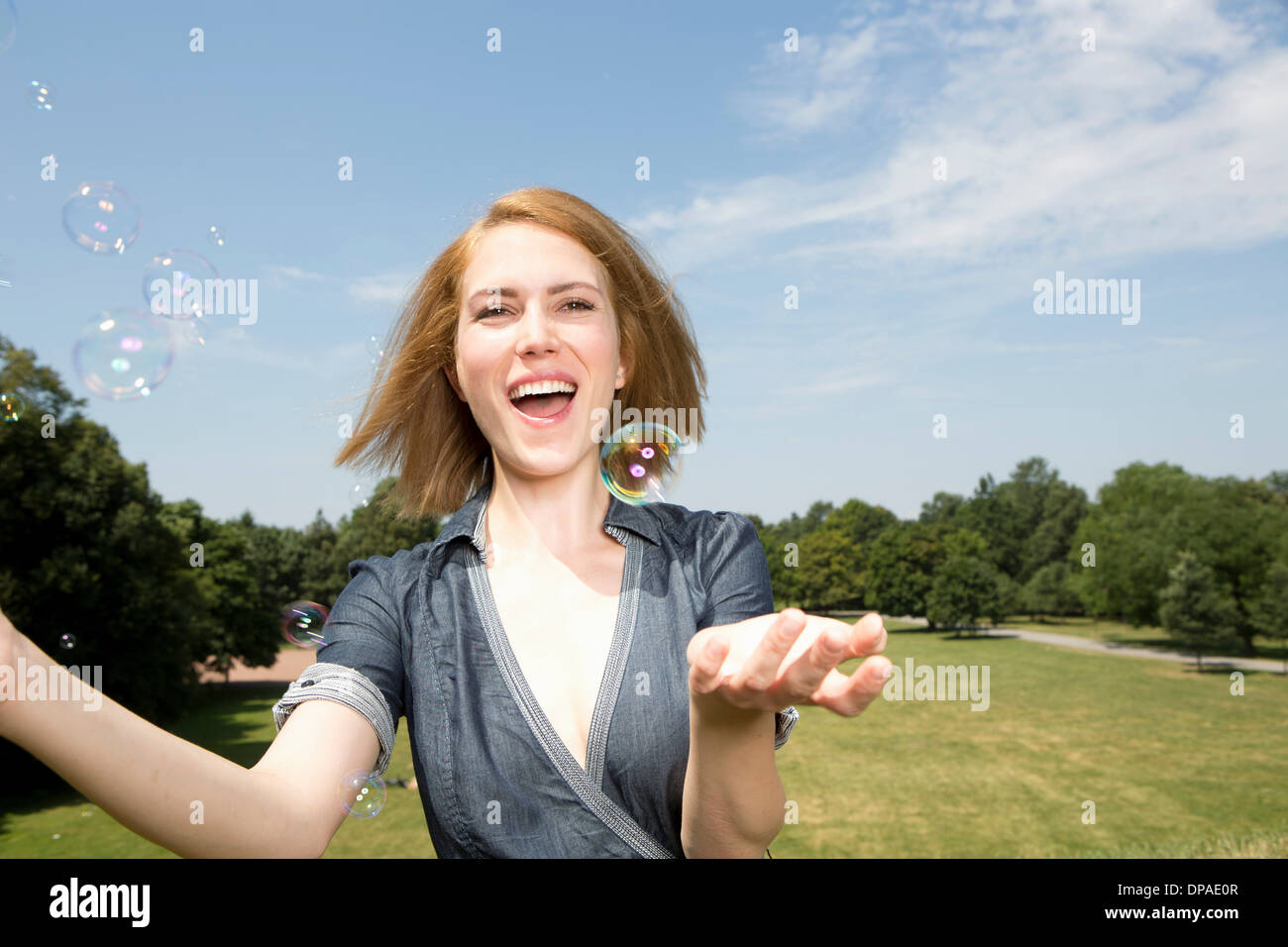 Young woman having fun with bubbles in park Stock Photo