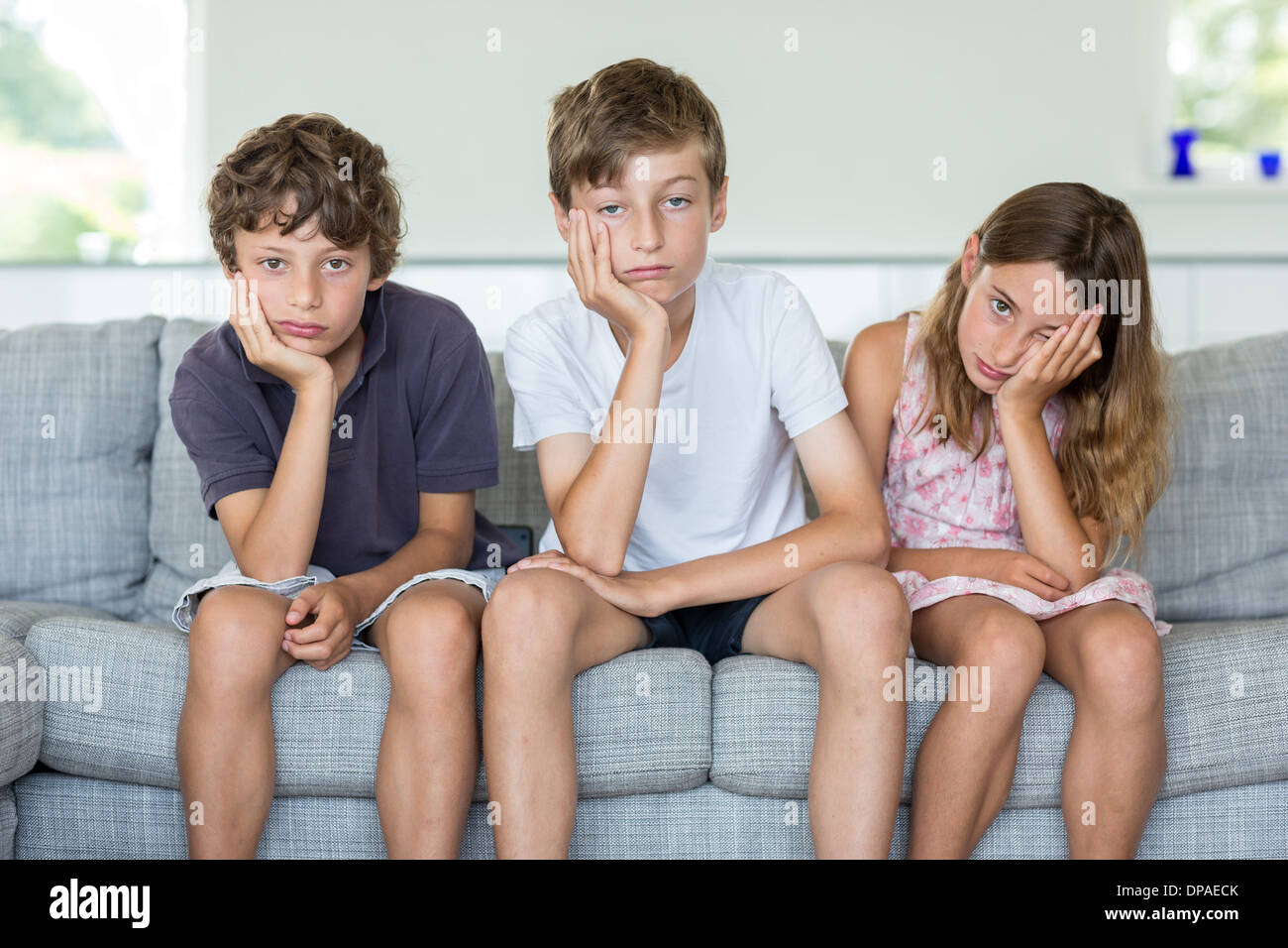 Brothers and sister on sofa looking bored Stock Photo