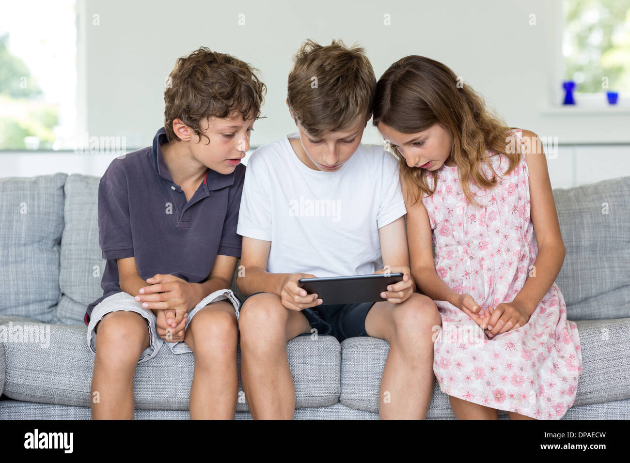 Brothers and sister on sofa looking at digital tablet Stock Photo