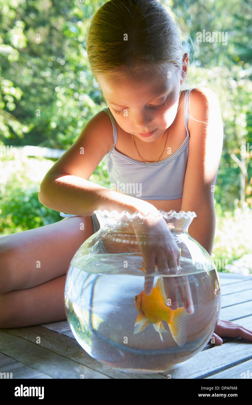 Young girl with fingers in goldfish bowl Stock Photo