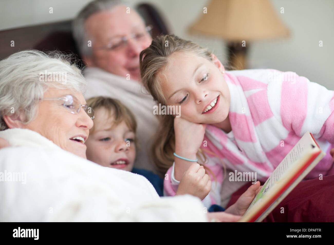 Grandparents and grandchildren reading storybook in bed Stock Photo