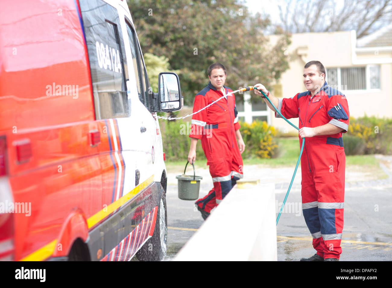 Paramedics cleaning ambulance with hosepipe Stock Photo