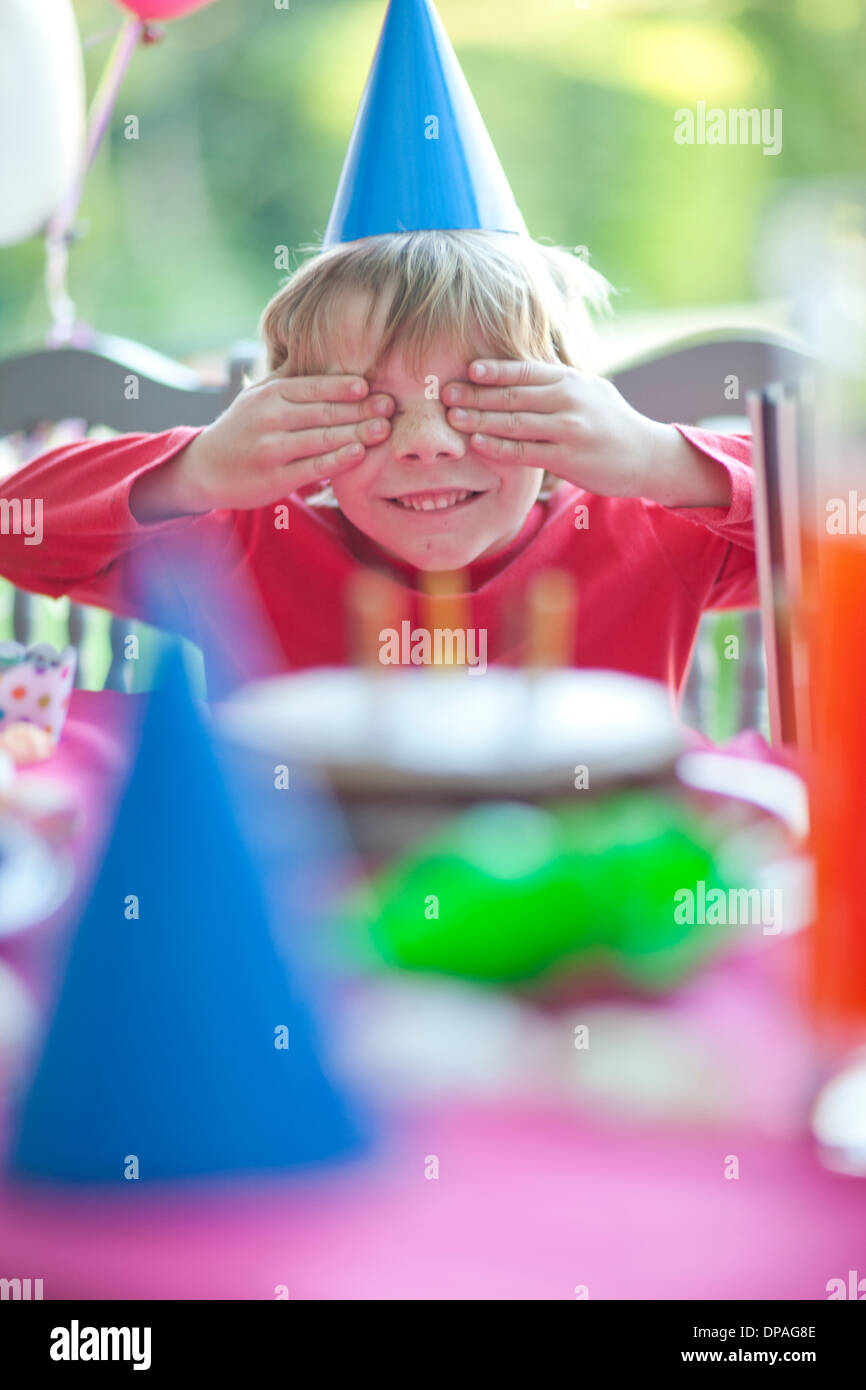 Young boy with hands over eyes at birthday party Stock Photo