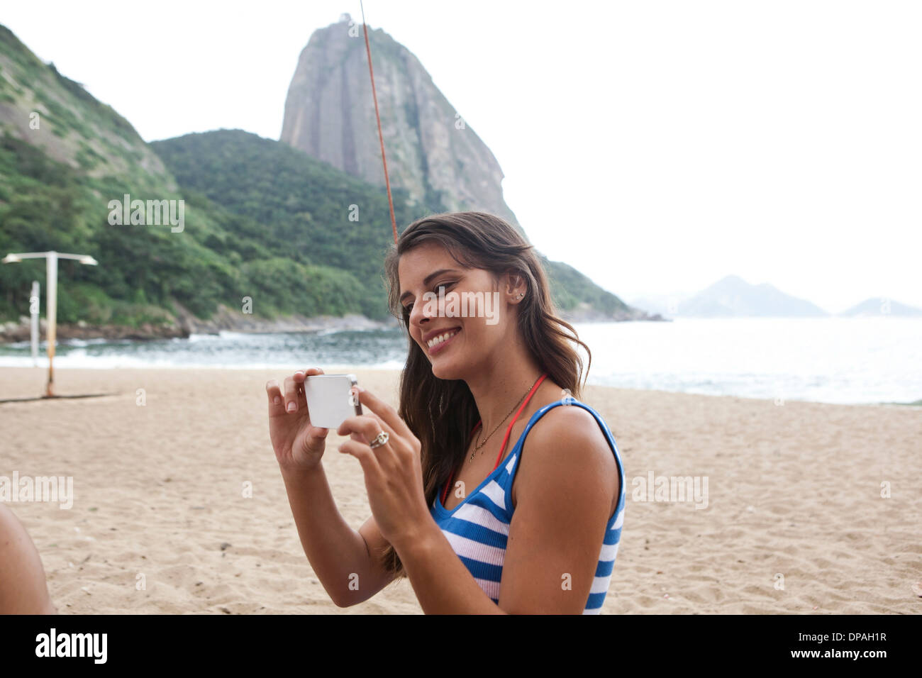 Woman using camera phone on beach, Rio de Janeiro, Brazil Stock Photo