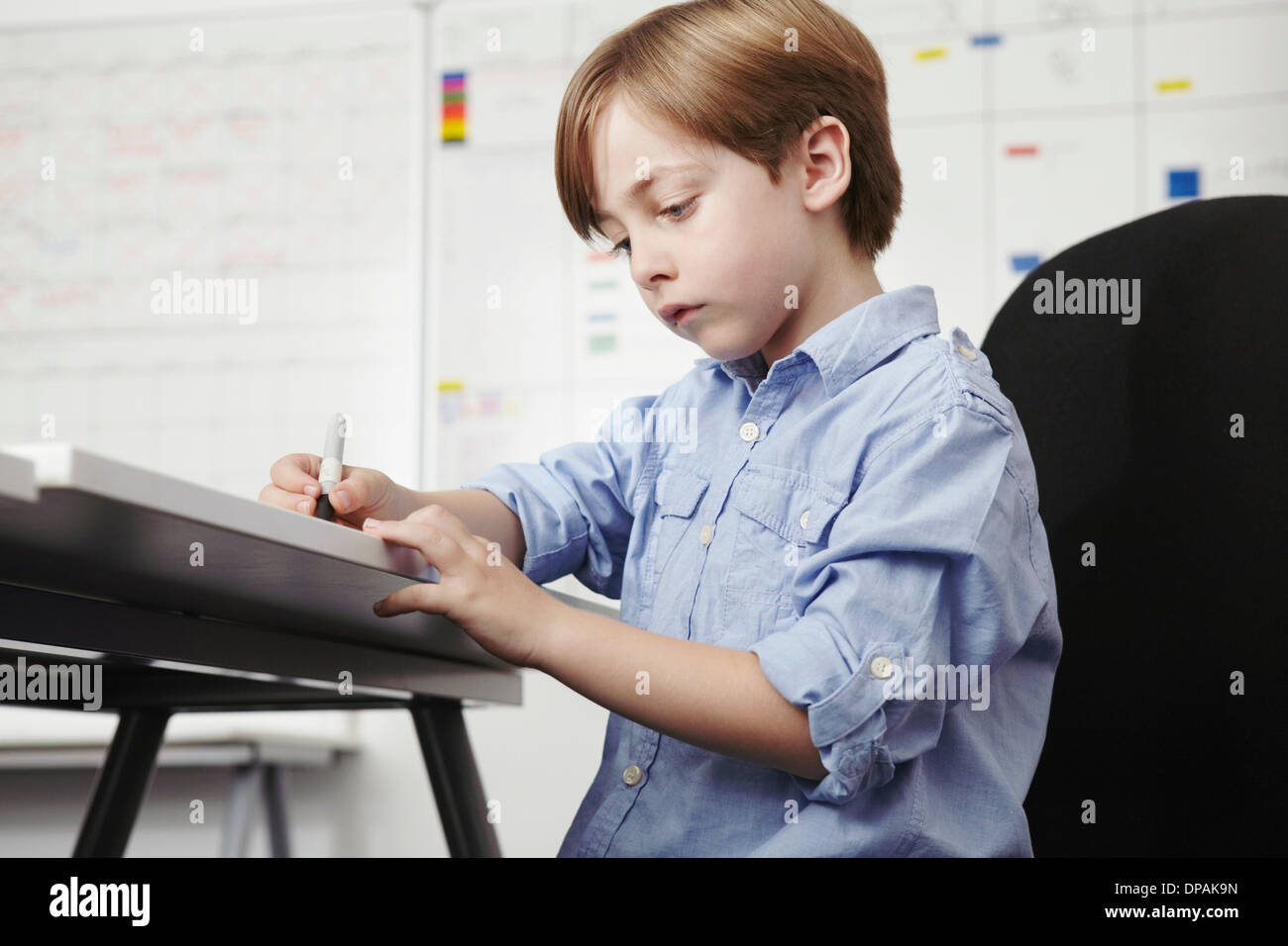 Boy writing at desk in office Stock Photo