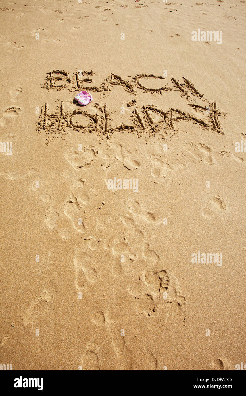 Messages and words written in the sand on a beach with kids crocs in pink and blue in picture. Topical for travel agents and holidays Stock Photo