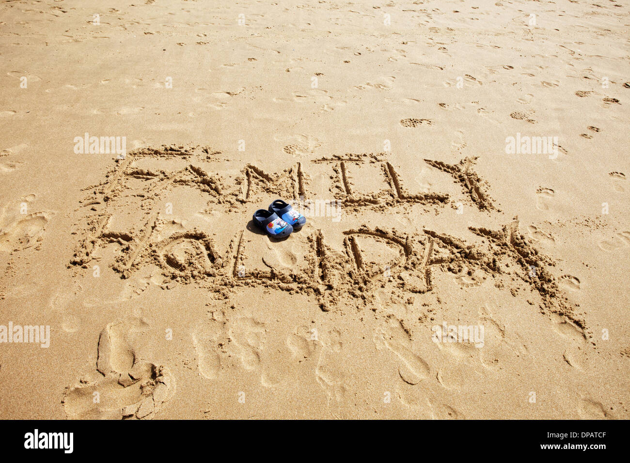 Messages and words written in the sand on a beach with kids crocs in pink and blue in picture. Topical for travel agents and holidays Stock Photo