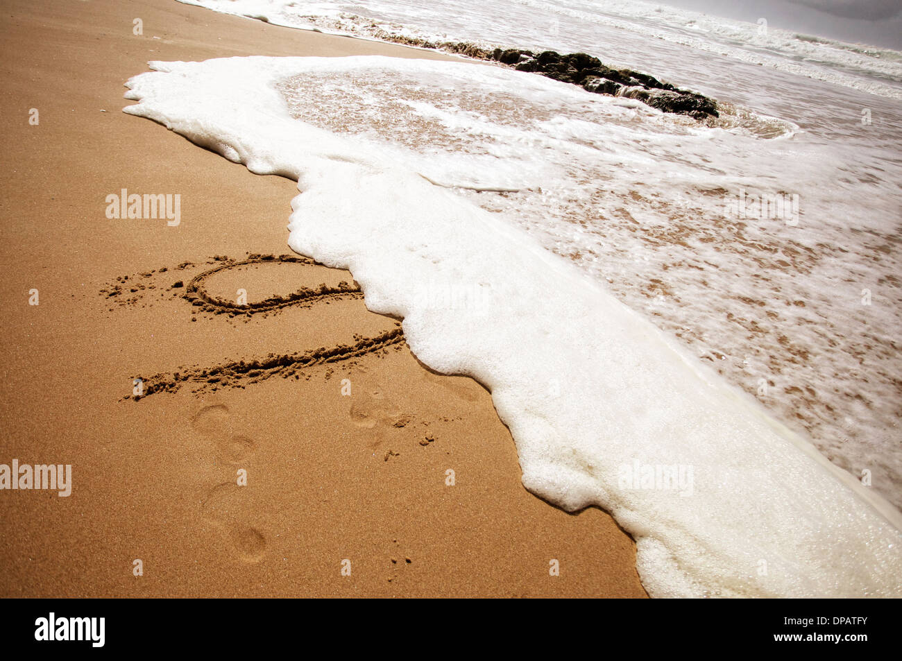 Holiday messages written into sand on a beach being washed away by the surf and waves coming ashore Stock Photo