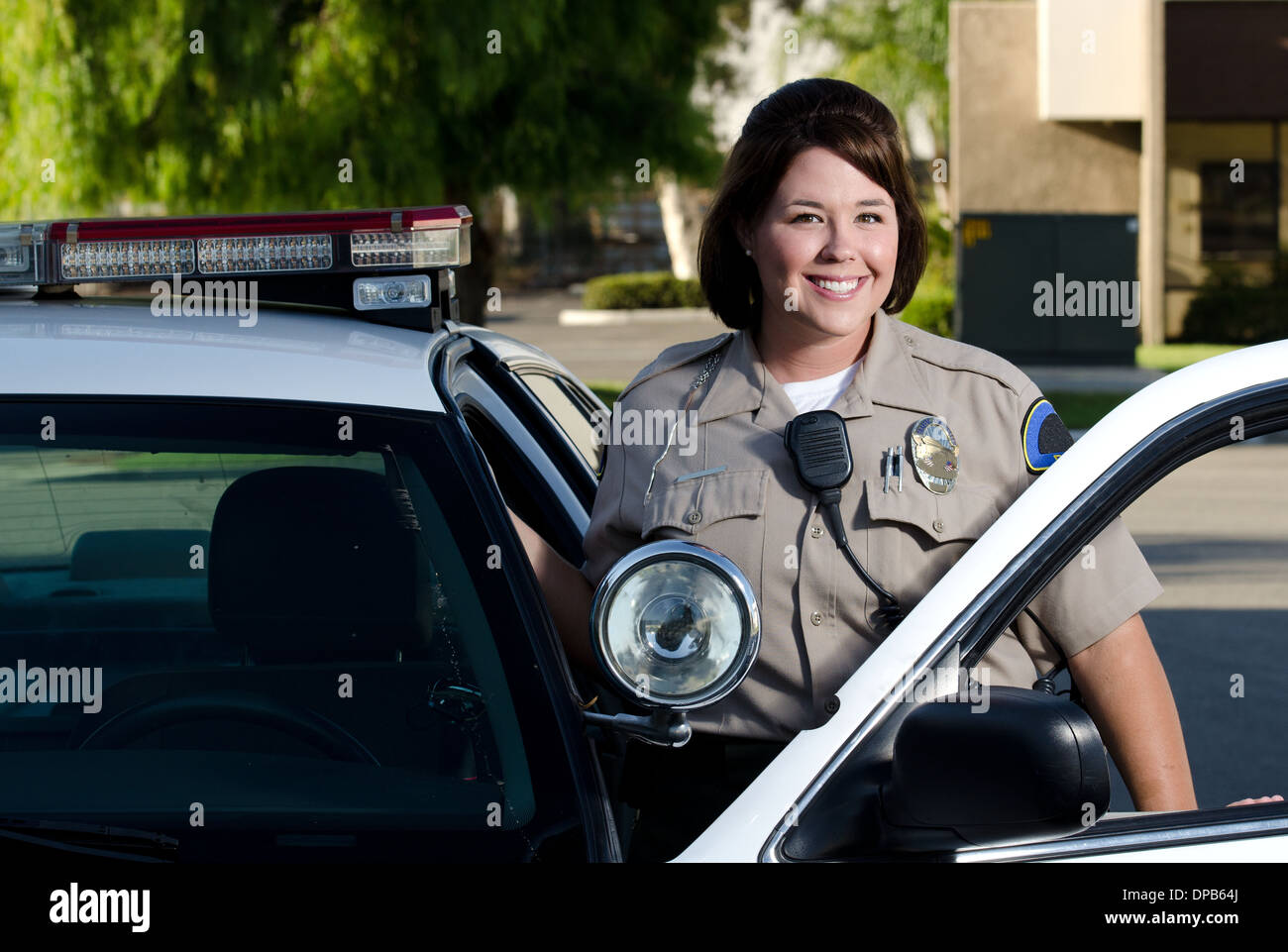 a friendly looking police officer smiles and stands next to her patrol car. Stock Photo